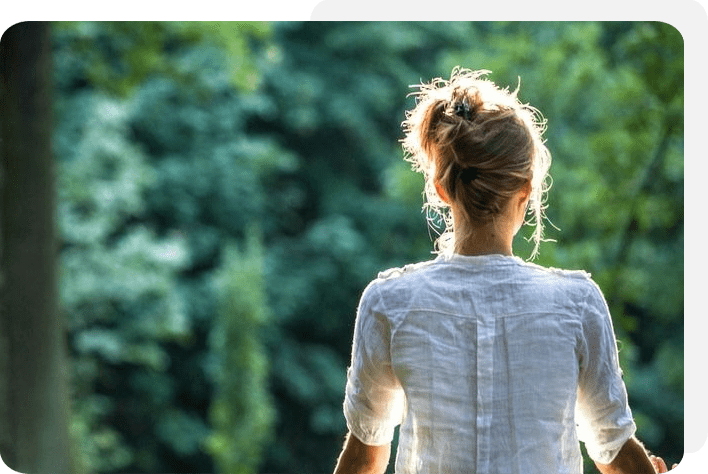 A woman in white shirt looking at trees.